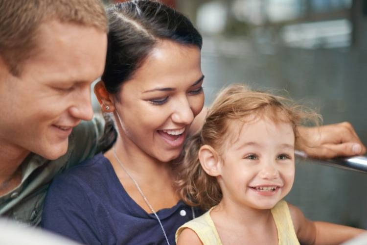 A dad, a mom, and a young girl smile while riding Disneyland park rides.