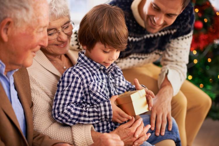 Grandparents and a dad surrounding a young boy as he looks at small gift box containing an unofficial invite to a Disneyland vacation in Anaheim.